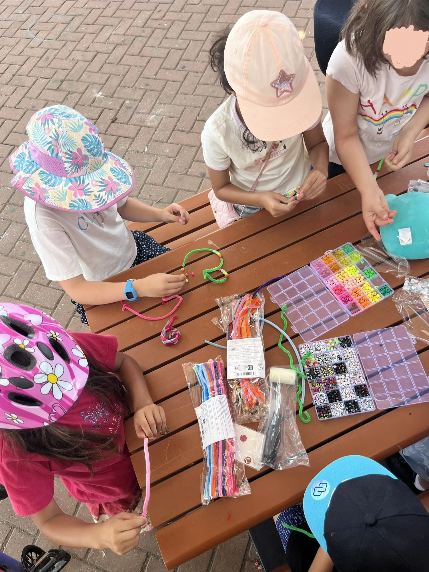 Children making bead and pipe-cleaner crafts together at an outdoor table